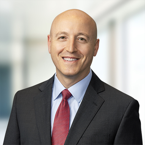 Bald man in a dark suit, light blue shirt, and red tie, smiling, stands in a bright, blurred office setting—representing chicago lawyers with expertise in litigation support.