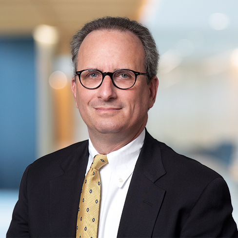 A middle-aged man with short gray hair and glasses, wearing a black suit, white shirt, and yellow patterned tie, poses in an office setting, reflecting the professionalism of top Chicago lawyers.