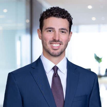 A man in a navy suit, white shirt, and tie smiles while standing in a bright corporate law office with glass walls—an example of professionalism among top lawyers in Chicago.