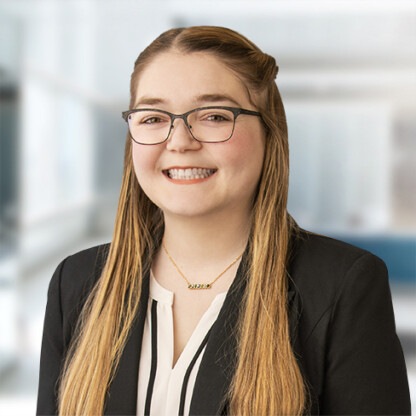 A woman with long blonde hair, glasses, and a black blazer smiles at the camera in a law office, reflecting the welcoming atmosphere of lawyers in Chicago.