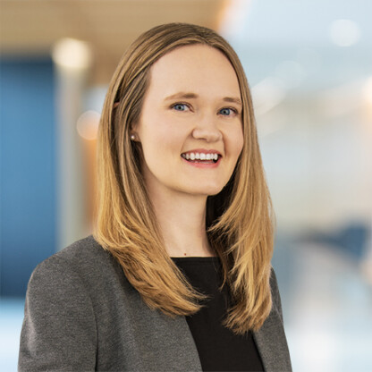 A woman with straight blonde hair wearing a gray blazer and black top smiles in a brightly lit corporate law office, showcasing the professional atmosphere of lawyers in Chicago.