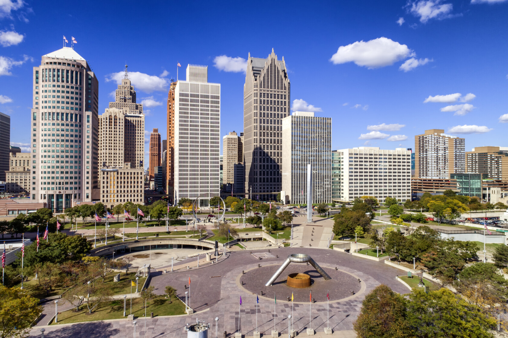 Aerial view of downtown Detroit featuring tall skyscrapers, the circular Hart Plaza, and clear blue skies with scattered clouds, highlighting the city’s vibrant atmosphere perfect for a corporate law office.