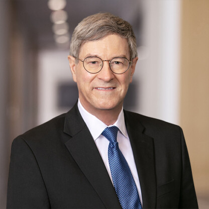An older man with gray hair and glasses, possibly one of the leading lawyers in Chicago, wears a dark suit, white shirt, and blue patterned tie, standing in a hallway with blurred lights in the background.