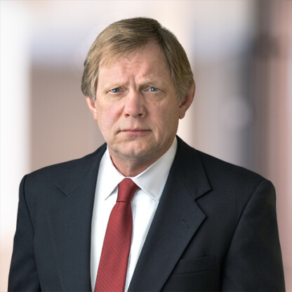 Man in a dark suit, white shirt, and red tie stands facing the camera against a blurred indoor background, reflecting the professional image of Chicago lawyers.