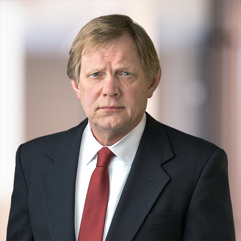 Man in a dark suit, white shirt, and red tie stands facing the camera against a blurred indoor background, reflecting the professional image of Chicago lawyers.