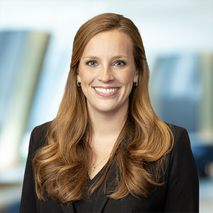 A woman with long, wavy auburn hair wearing a black blazer smiles at the camera in a modern corporate law office, reflecting the professionalism of Chicago lawyers specializing in litigation support.