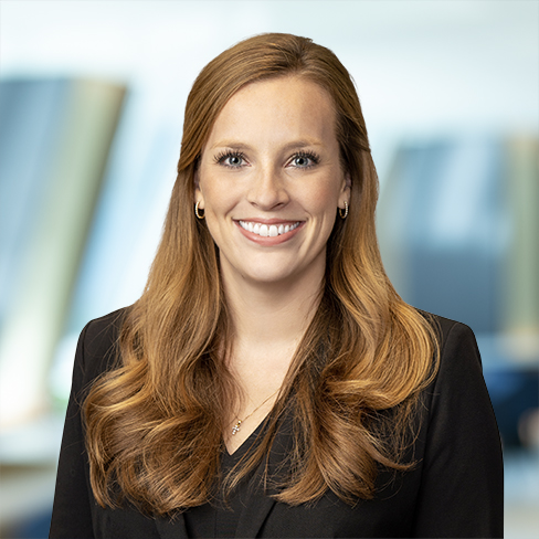 A woman with long, wavy auburn hair wearing a black blazer smiles at the camera in a modern corporate law office, reflecting the professionalism of Chicago lawyers specializing in litigation support.