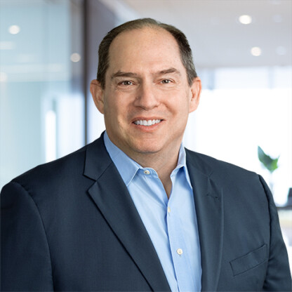 A man in a blue suit and light blue shirt smiles while standing in a modern, well-lit office environment, representing Chicago lawyers known for their expertise in intellectual property law.