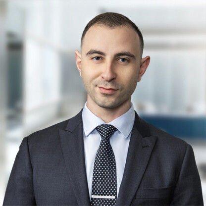 A man in a suit and tie stands in a modern, blurred office setting, facing the camera with a neutral expression—typical of lawyers in Chicago offering professional litigation support.