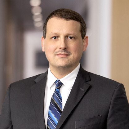 Man in a dark suit and striped tie standing in a hallway with a neutral expression, blurred background—ideal for representing litigation support or lawyers in Chicago.