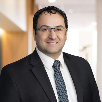 Man in business attire with glasses, dark hair, and a patterned tie, smiling in a law offices hallway—representing lawyers in Chicago specializing in intellectual property law.
