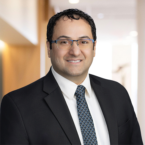 Man in business attire with glasses, dark hair, and a patterned tie, smiling in a law offices hallway—representing lawyers in Chicago specializing in intellectual property law.