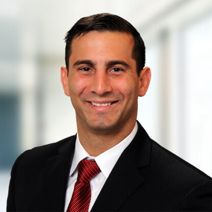 A man in a dark suit, white shirt, and red striped tie smiles at the camera against a blurred indoor background, representing chicago lawyers with expertise in intellectual property law.