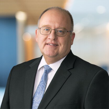 A man in a suit, dress shirt, and patterned tie stands in a blurred indoor setting, looking at the camera and smiling slightly—reflecting the professionalism found in top Chicago lawyers and law offices.