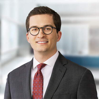 A man wearing glasses, a dark suit, a white shirt, and a red patterned tie stands in a modern office setting, embodying the professionalism of top Chicago lawyers.