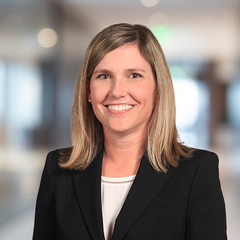 Woman with straight, shoulder-length blonde hair wearing a black blazer and white top, smiling, in a blurred office setting—ideal for Chicago lawyers or those providing litigation support.