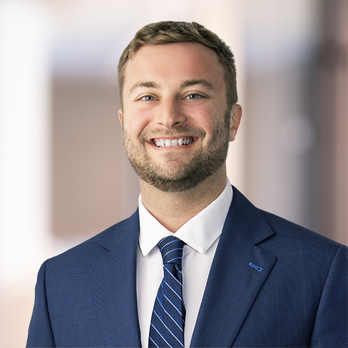 Smiling man wearing a blue suit, white shirt, and striped blue tie, standing in front of a blurred indoor background, representing chicago lawyers with expertise in intellectual property law.