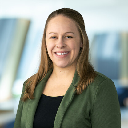 Woman with straight light brown hair, wearing a green blazer and black top, smiling at the camera with a blurred office background—perfect for showcasing litigation support or highlighting top lawyers in Chicago.