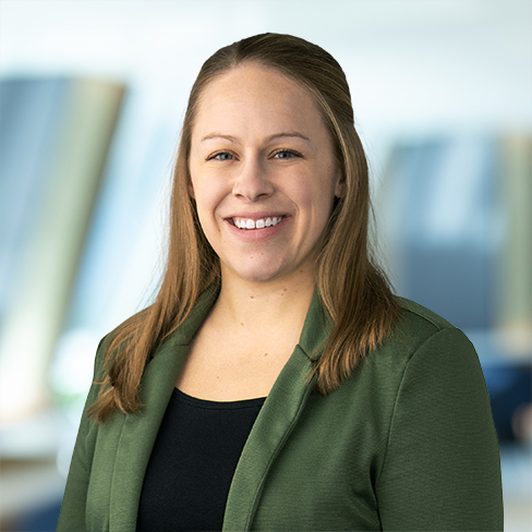 Woman with straight light brown hair, wearing a green blazer and black top, smiling at the camera with a blurred office background—perfect for showcasing litigation support or highlighting top lawyers in Chicago.