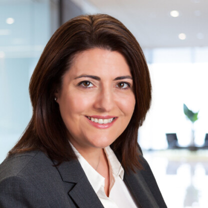 A woman with medium-length brown hair wearing a gray blazer and white shirt, smiling at the camera in a modern corporate law office alongside other experienced lawyers in Chicago.