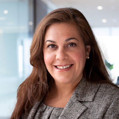 Woman with long brown hair wearing a grey blazer smiles at the camera in a modern, well-lit law office, reflecting the professionalism of top lawyers in Chicago.
