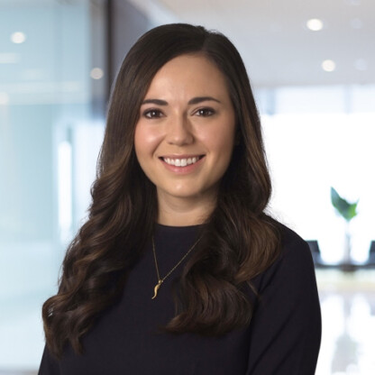 A woman with long brown hair, wearing a dark top and a gold necklace, smiles at the camera in a modern law office, reflecting the professional atmosphere of lawyers in Chicago.