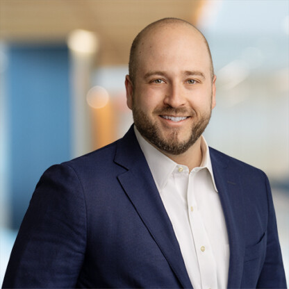 A man in a navy blue suit and white shirt smiles at the camera in a modern, blurred office setting, reflecting the professionalism found in top law offices.
