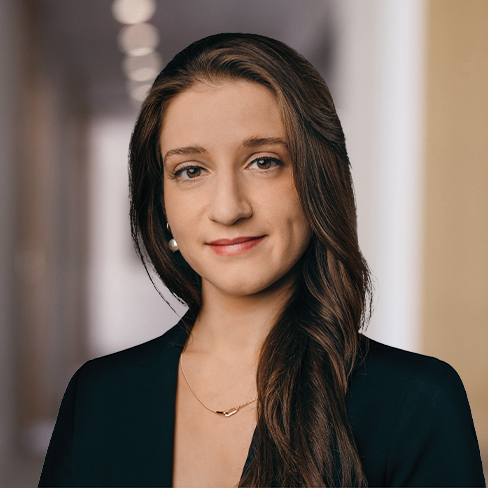 A woman with long brown hair in a dark blazer and necklace stands in a hallway with blurred lights, reflecting the professionalism often seen in law offices specializing in intellectual property law.
