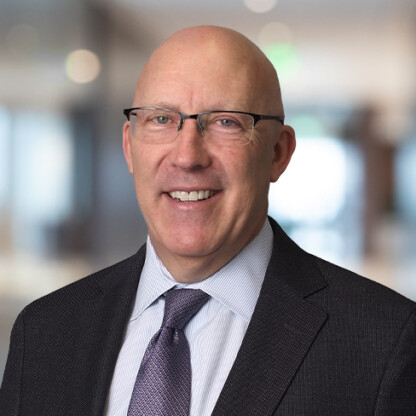 A bald man wearing glasses, a suit jacket, a dress shirt, and a tie, standing indoors with a blurred office background—ideal for profiles of Chicago lawyers specializing in litigation support.