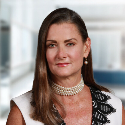Woman with long brown hair wearing a pearl choker necklace, pearl earring, and a white top with black lace detailing, posed in a bright, modern indoor setting—perfect for professional profiles like lawyers in Chicago.