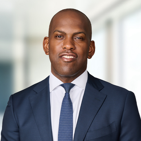 A man wearing a dark blue suit, white shirt, and blue polka dot tie stands in front of a blurred office background, representing lawyers in Chicago who specialize in intellectual property law.