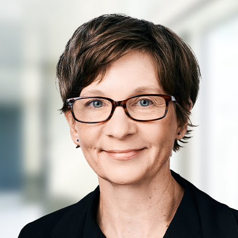 A person with short brown hair, glasses, and a black jacket, smiling slightly in front of a blurred indoor background of a corporate law office for chicago lawyers.