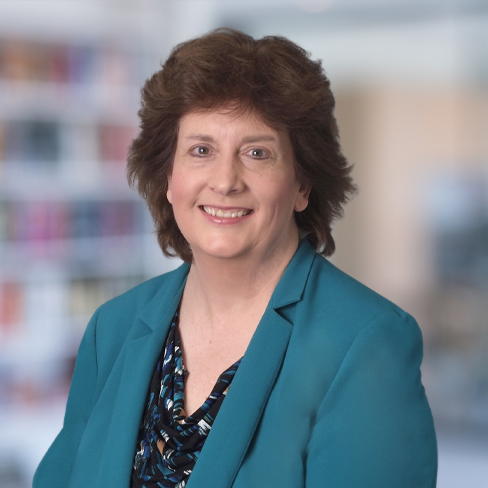 A middle-aged woman with short brown hair wearing a teal blazer and patterned blouse, smiling at the camera in an office setting, representing Chicago lawyers with expertise in litigation support.