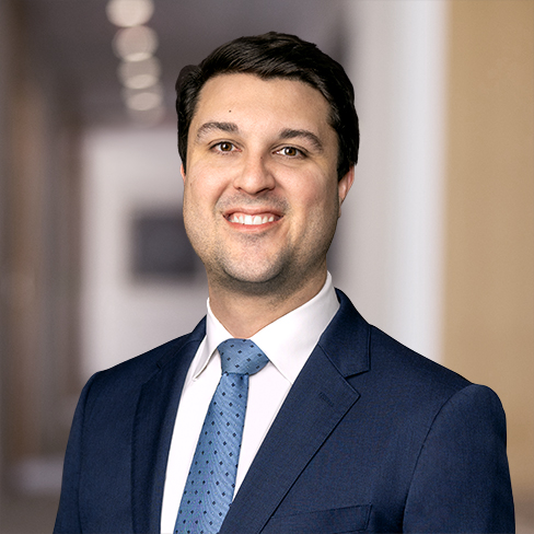 A man in a dark blue suit and tie smiles at the camera, standing in a blurred indoor hallway with soft lighting—typical of a corporate law office frequented by Chicago lawyers.