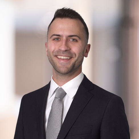 A man in a dark suit, white shirt, and patterned tie is smiling while standing in front of a blurred indoor background, reflecting the professionalism often seen among lawyers in Chicago.