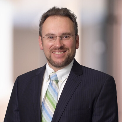Man in a dark pinstripe suit, white shirt, and striped tie, standing and smiling in front of a blurred indoor background—an embodiment of Chicago lawyers experienced in litigation support.