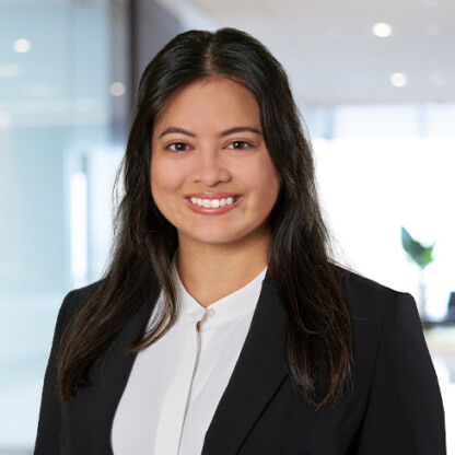 A woman with long dark hair, wearing a black blazer and white blouse, smiles in a modern office setting with glass walls—reflecting the professionalism of Chicago lawyers in intellectual property law.