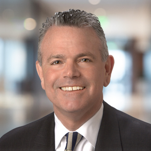 Smiling man in a business suit and tie with short gray hair, posing in a blurred office setting, representing experienced lawyers in Chicago.