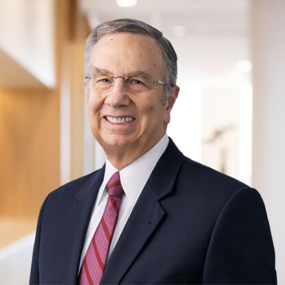 Smiling older man with glasses, gray hair, and a suit with a red striped tie, standing in a bright office hallway at one of the top law offices for Chicago lawyers.