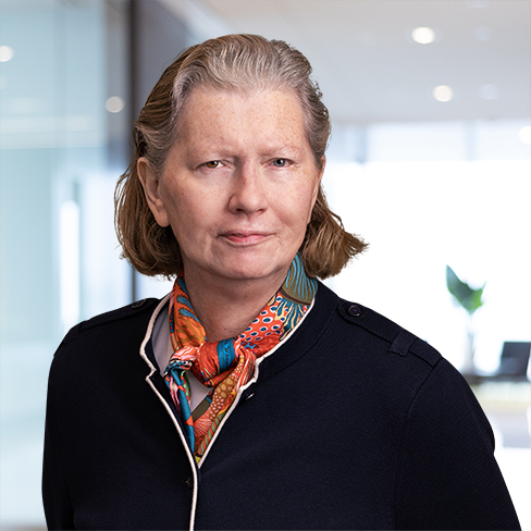 A middle-aged woman with light skin and short, light brown hair, wearing a dark jacket and a colorful scarf, stands in a modern office setting known for Chicago lawyers specializing in intellectual property law.