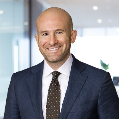 A bald man in a navy suit and polka dot tie smiles while standing in a modern, bright corporate law office, reflecting the professional atmosphere of top lawyers in Chicago.