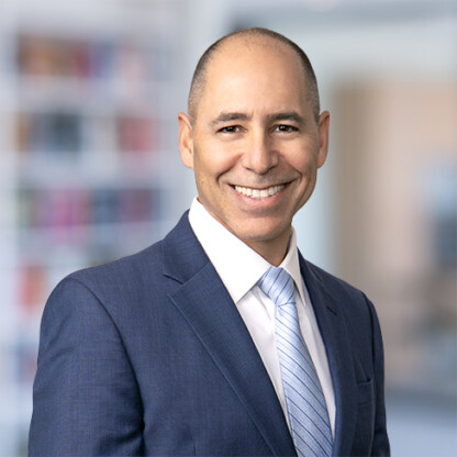 Smiling man in a blue suit, white shirt, and light blue tie stands in front of a blurred office background, representing Chicago lawyers dedicated to providing expert litigation support.