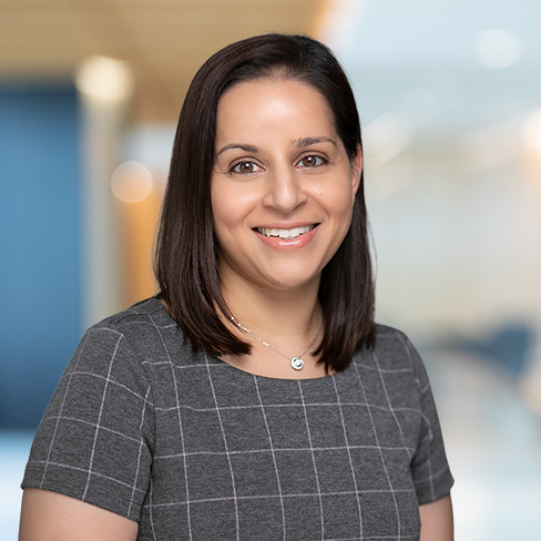 A woman with straight dark hair and a patterned grey dress smiles at the camera in a corporate law office, reflecting the professional atmosphere of top lawyers in Chicago.