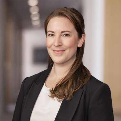 A woman wearing a black blazer and white top stands indoors, smiling slightly, with a blurred hallway in the background—reflecting the professionalism of Chicago lawyers.