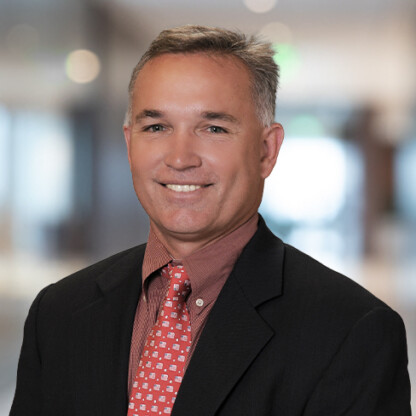 Man in a dark suit and patterned red tie smiling, standing in a blurred indoor office setting, representing chicago lawyers experienced in intellectual property law.