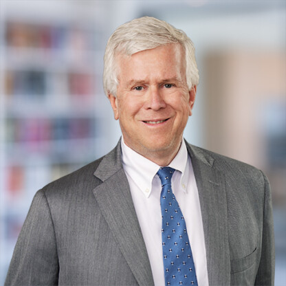 A middle-aged man with white hair wearing a gray suit, white shirt, and blue patterned tie, stands in front of a blurred corporate law office, representing the professionalism of lawyers in Chicago.