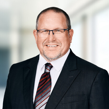 A middle-aged man wearing glasses, a dark suit, white shirt, and striped tie, smiling in a modern, blurred corporate law office—ideal for profiles of top Chicago lawyers.
