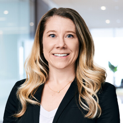 A woman with long blonde hair wearing a black blazer and white top smiles at the camera in a modern corporate law office, reflecting the professional atmosphere of Chicago lawyers and their litigation support teams.