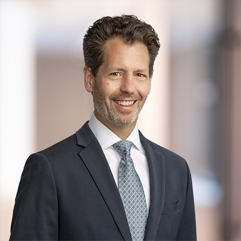 A man in a suit and tie is standing and smiling at the camera with a blurred indoor background, representing dedicated lawyers in Chicago from leading law offices.