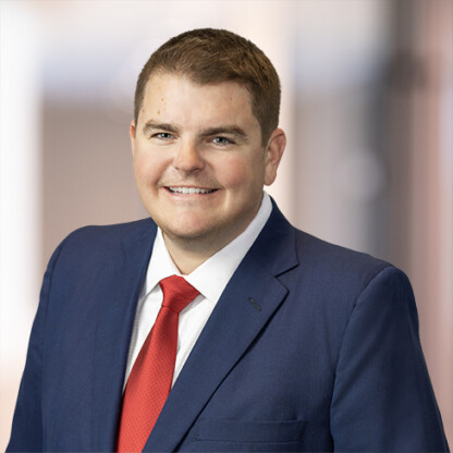Man in a blue suit and red tie smiling in front of a blurred indoor background, representing the professionalism of top law offices and lawyers in Chicago.